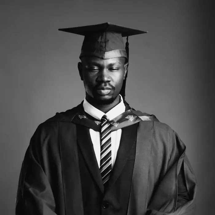 A graduate in cap and gown looking down, photographed in black and white
