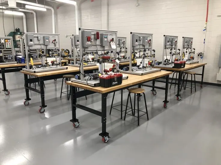 Electrical training benches with wiring panels, batteries and stools in a workshop