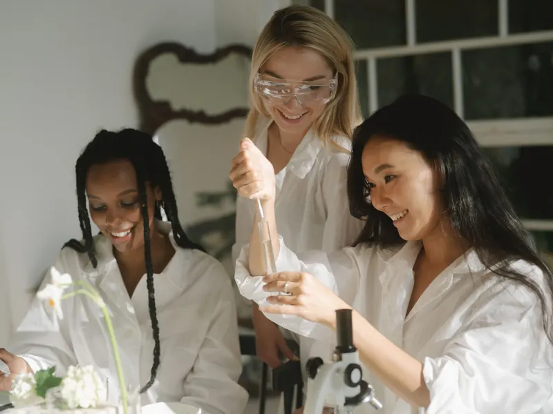 Three students in white coats carrying out a test tube experiment at a lab bench